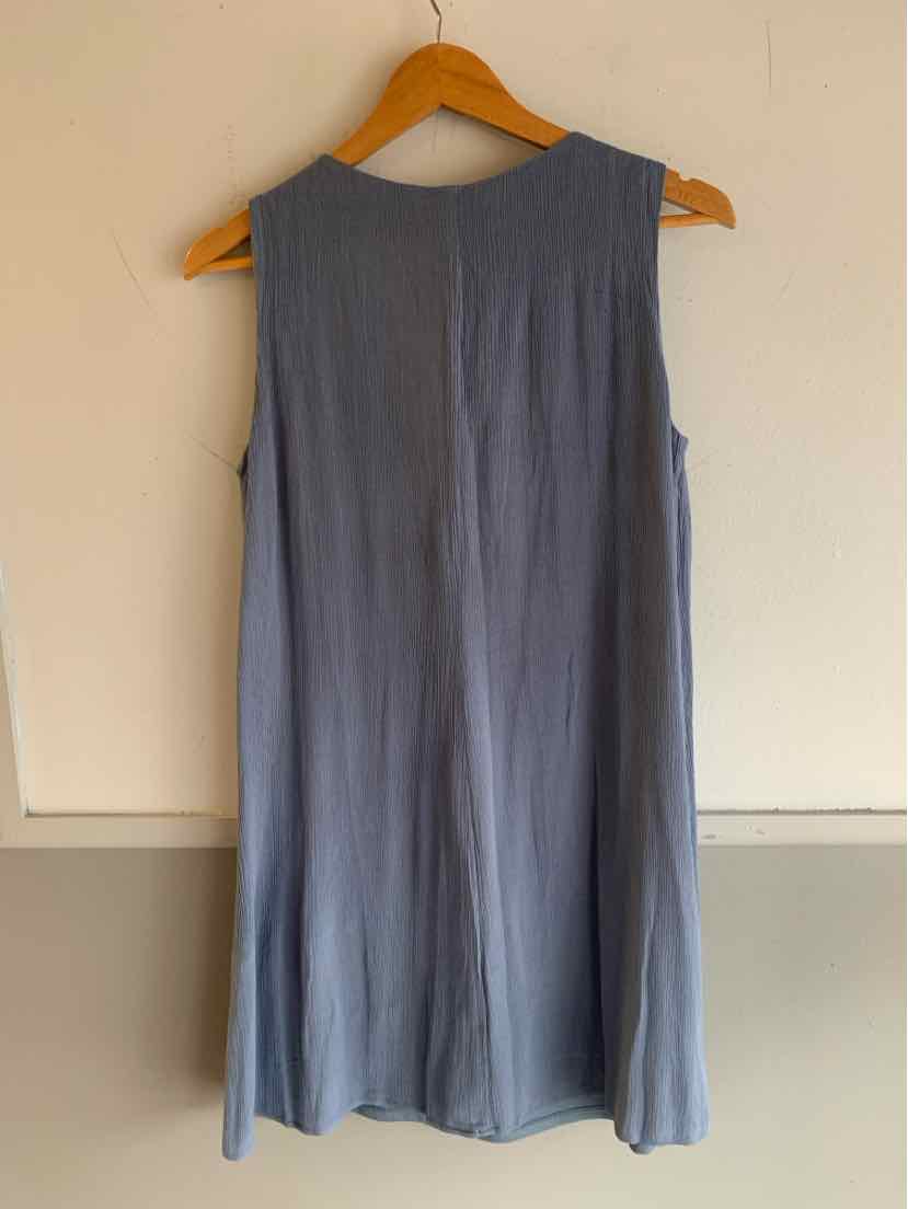 Sleeveless blue dress with a relaxed fit, hanging on wooden hanger against white wall.