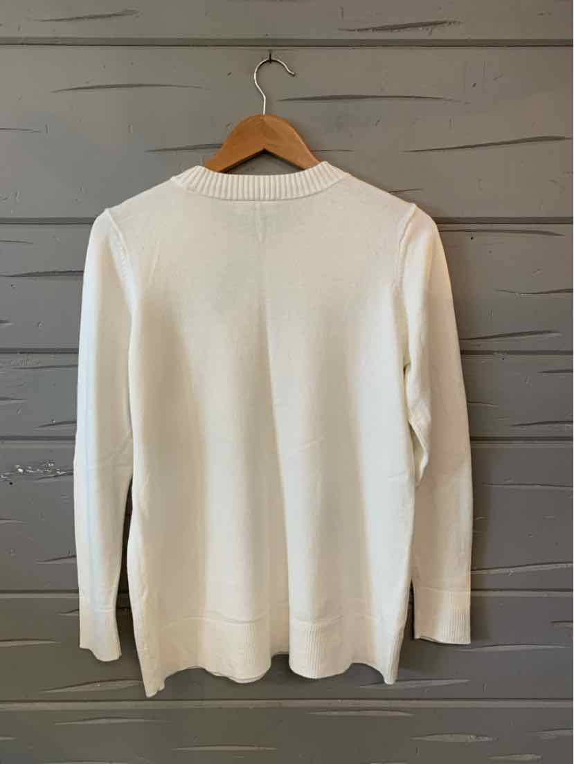 White long-sleeve knit sweater with crew neck, hanging on wooden hanger against gray wooden wall.