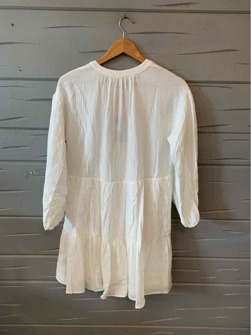 White long-sleeve dress with gathered waist and tiered skirt hanging on wooden hanger.
