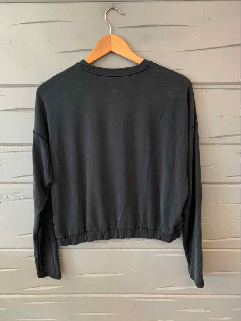 Black long-sleeve cropped sweatshirt with crew neckline and elastic hem hanging on wooden hanger.