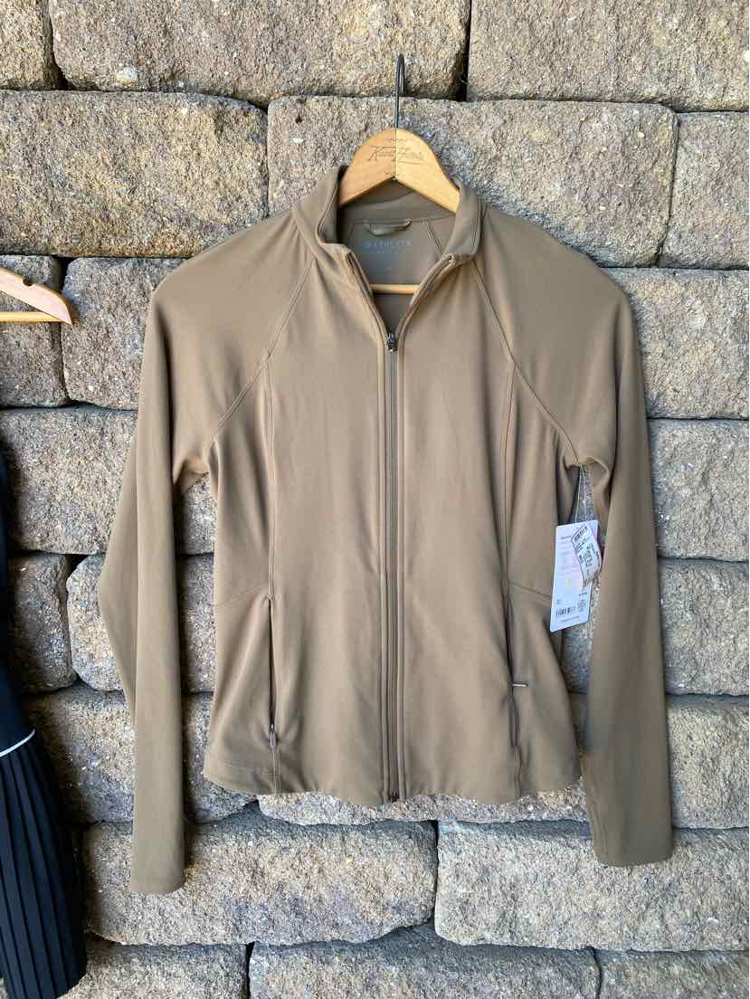 Light brown full-zip athletic jacket with long sleeves and stand collar on wooden hanger against stone wall.