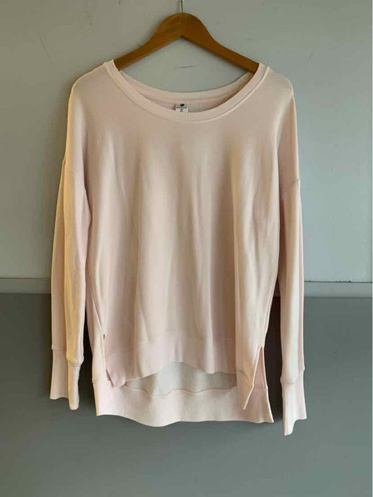 Light pink long-sleeve crewneck sweater with ribbed cuffs and side slits hanging on wooden hanger.