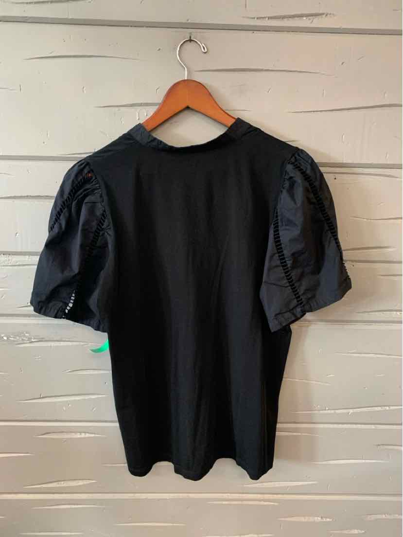 Black oversized T-shirt with shiny puff sleeves hanging on wooden hanger against white wooden wall.