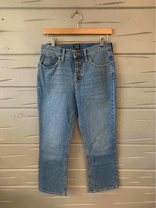 Blue denim jeans with button fly and raw hem, size 4, hanging on wooden hanger against beige wall.