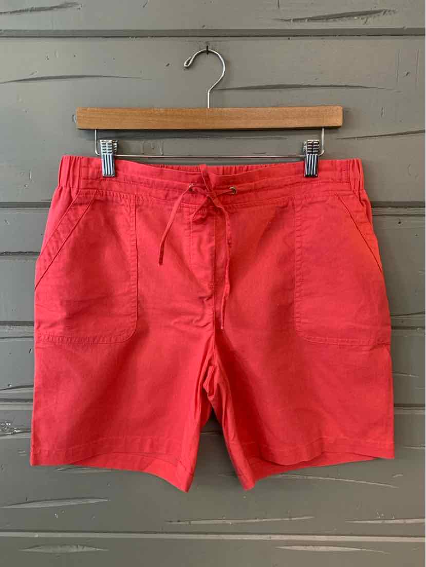 Coral red drawstring shorts with front pockets and a relaxed fit hanging on a wooden hanger against a gray wall.