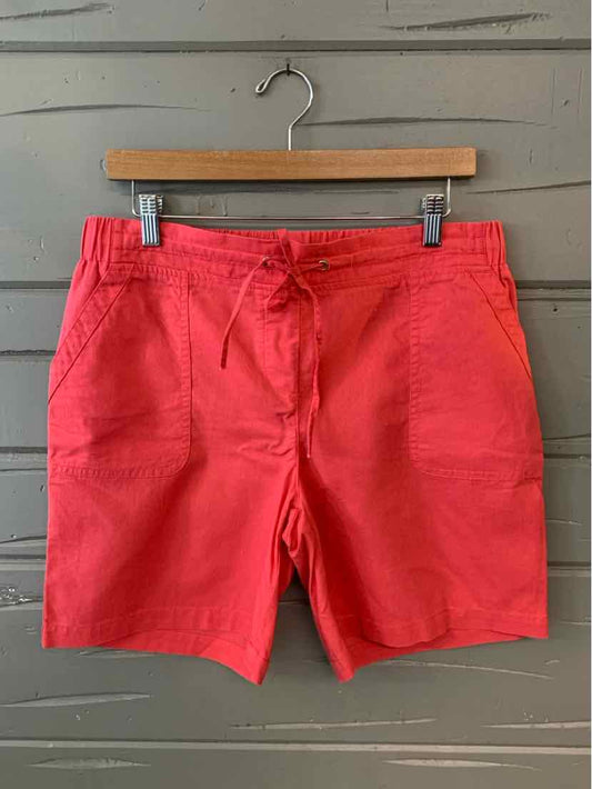 Coral red drawstring shorts with front pockets and a relaxed fit hanging on a wooden hanger against a gray wall.
