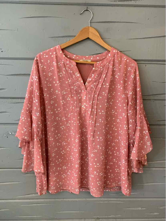 Pink oversized blouse with white floral pattern, V-neckline, and tiered ruffle sleeves.