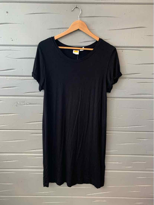 Black short-sleeve casual dress in large size hanging on wooden hanger against gray wooden wall.