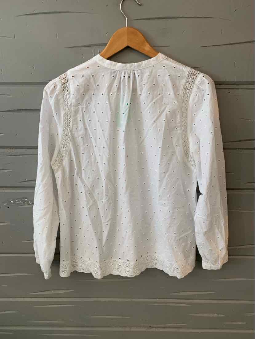 White long-sleeve eyelet blouse with delicate floral cutouts and buttoned cuffs hanging on wooden hanger.