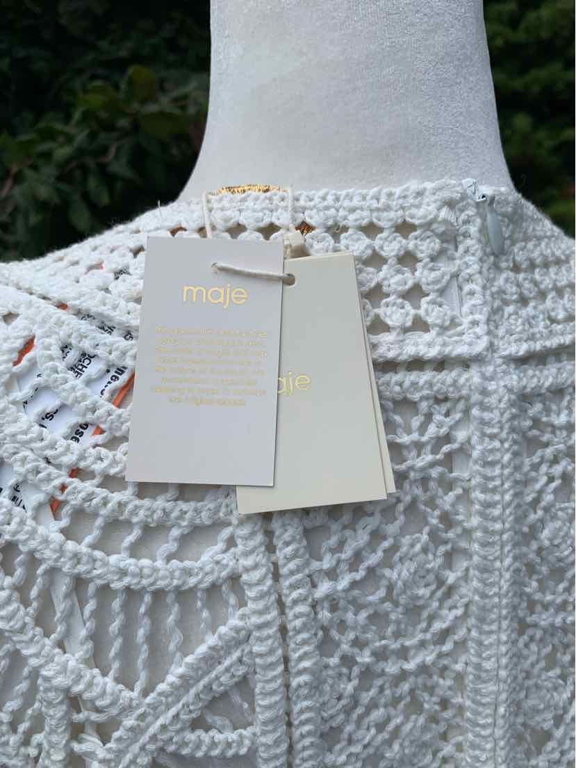White crocheted top with intricate openwork floral patterns and attached white tags with gold lettering.