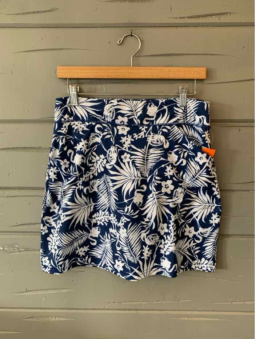 Navy blue skirt with white tropical leaf print, fitted waistband, and front pleats hanging on wooden hanger.
