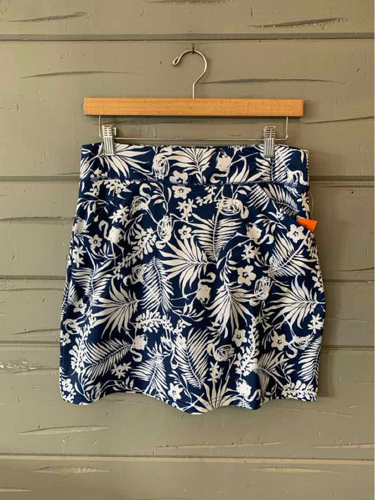 Navy blue skirt with white tropical leaf print, fitted waistband, and front pleats hanging on wooden hanger.