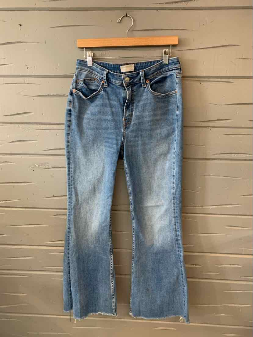 Blue denim jeans with slight fading, flared legs, front button closure, and five-pocket design hanging on a wooden hanger.