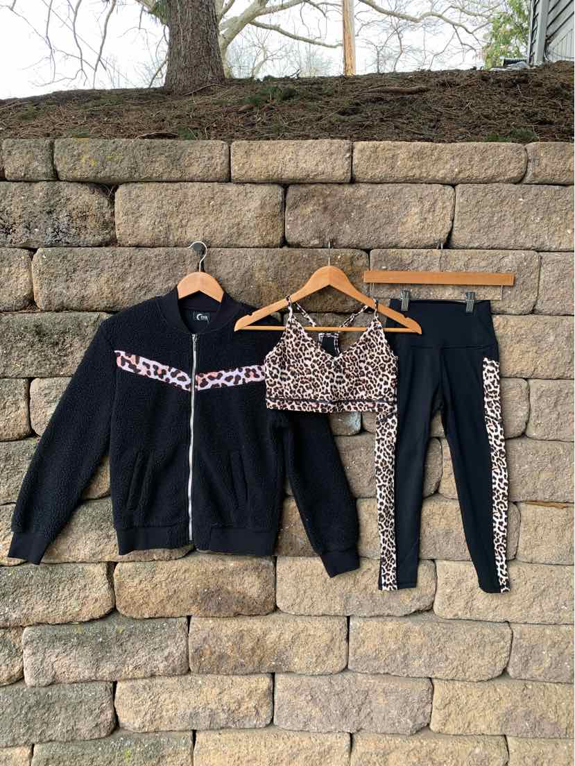 Black zip-up jacket, leopard print sports bra, and black leggings with leopard side stripes, all hanging on wooden hangers.