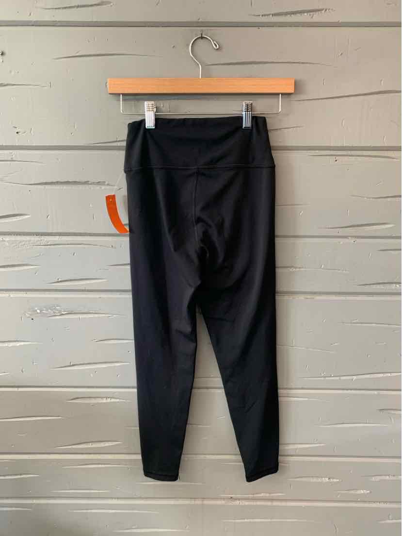 Black high-waisted leggings with a fitted ankle and smooth fabric hanging on wooden hanger against gray wall.