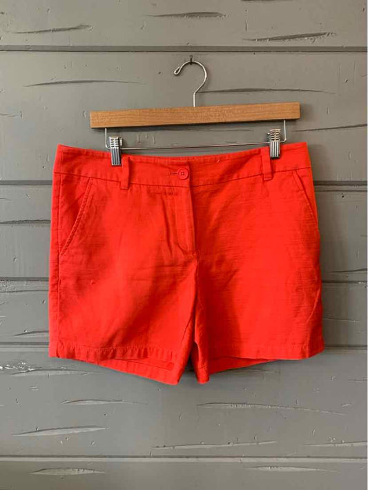 Bright red casual shorts with front pockets and belt loops hanging on wooden hanger against gray paneled wall.