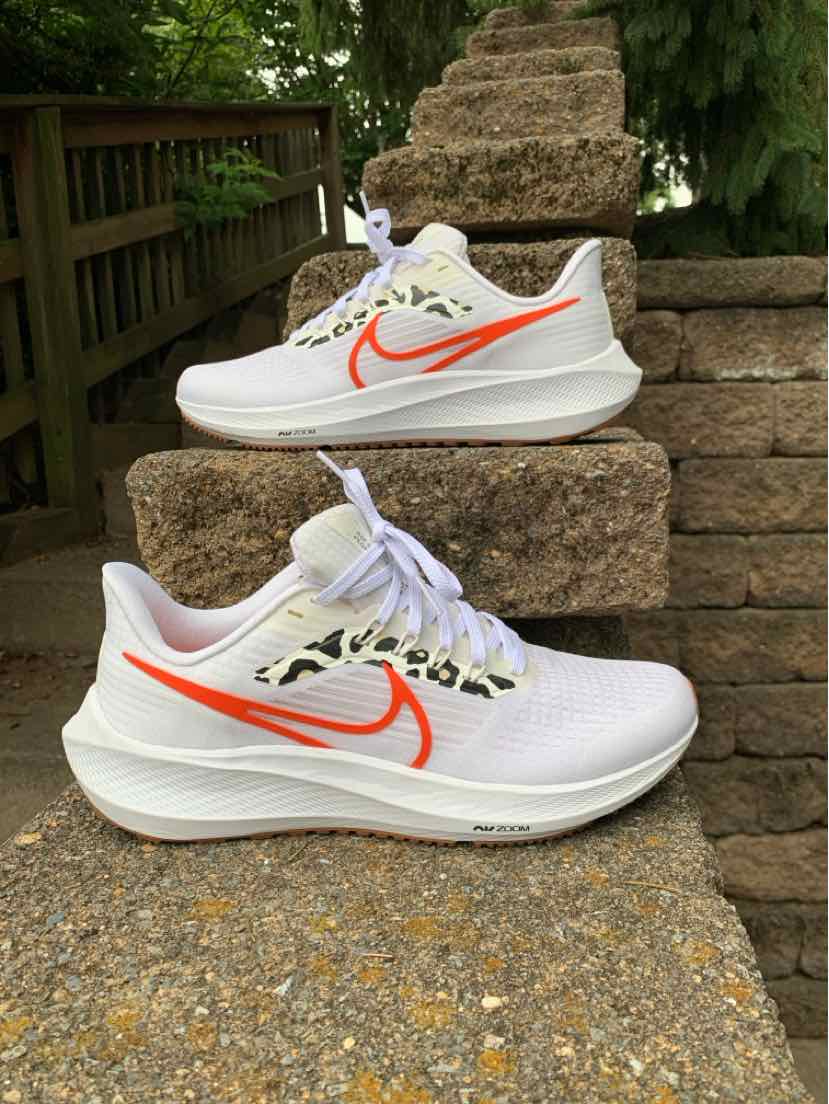 White Nike running sneakers with bright orange swoosh, leopard print eyelets, and white laces.
