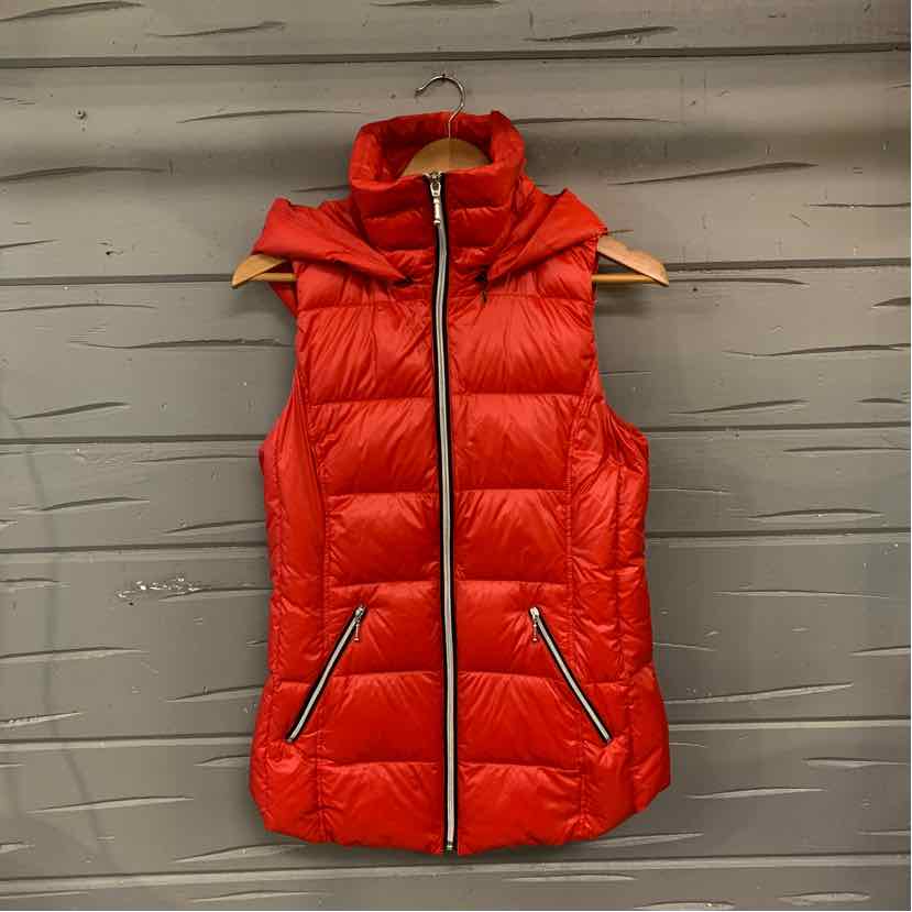Red quilted sleeveless anorak vest with front zipper and zippered pockets on wooden hanger.