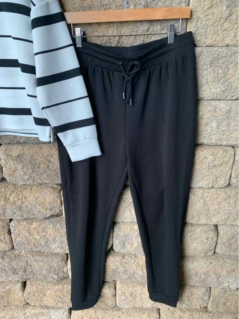 Black drawstring jogger pants with tapered legs hanging against a stone wall backdrop.