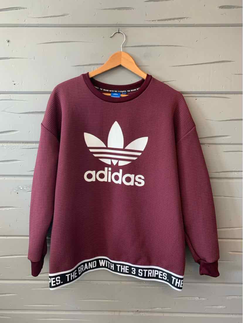 Burgundy crewneck sweatshirt with white adidas trefoil logo and black elastic hem featuring white branding text.