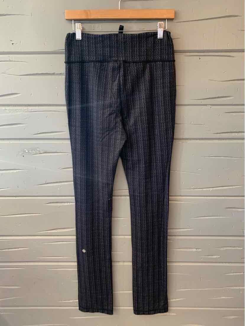 Black fitted leggings with subtle checkered pattern and high waistband hanging on wooden hanger.