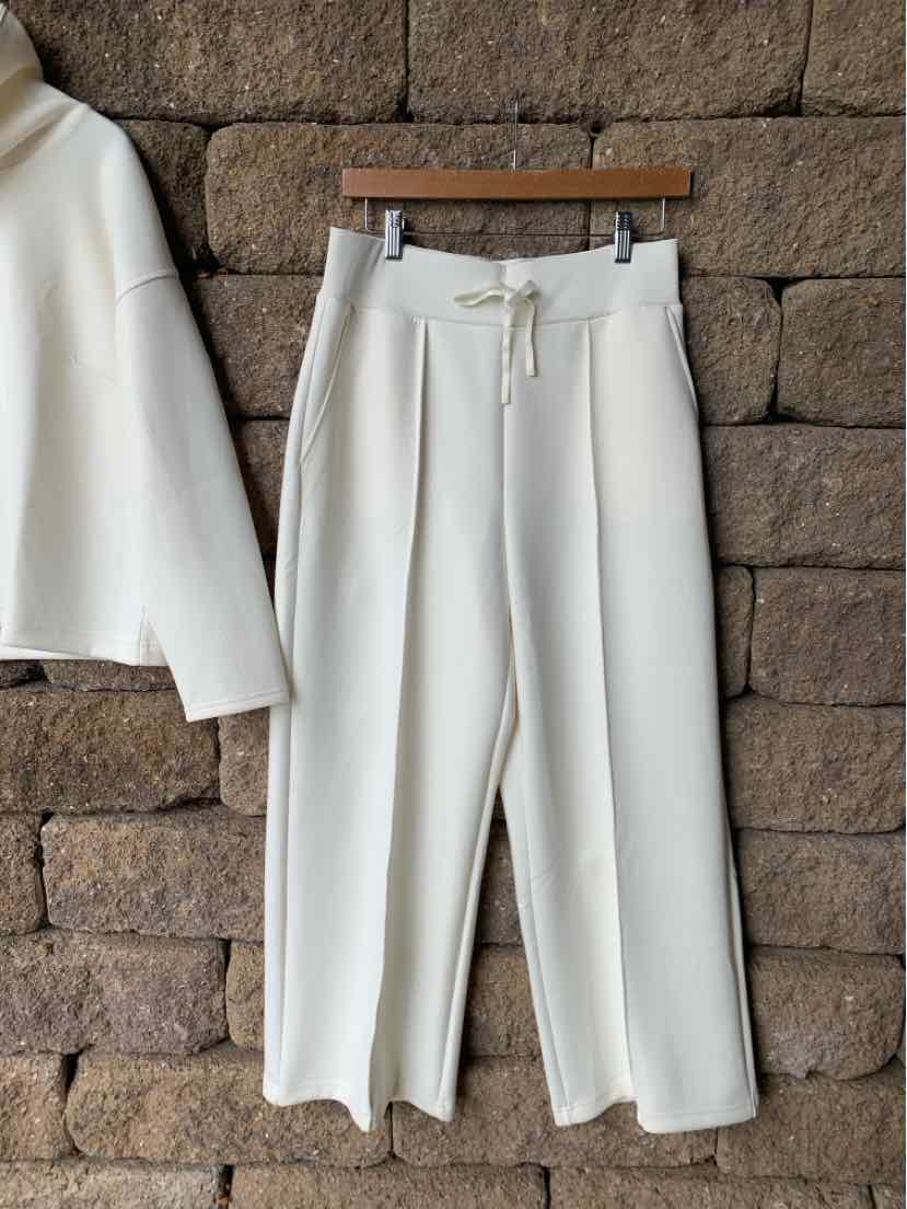 Cream-colored wide-leg pants with drawstring waist and front crease detail, hanging on wooden hanger.