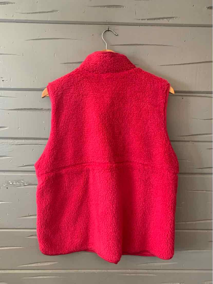 Bright red sleeveless sherpa vest with a stand collar and relaxed fit, hanging on wooden hanger.