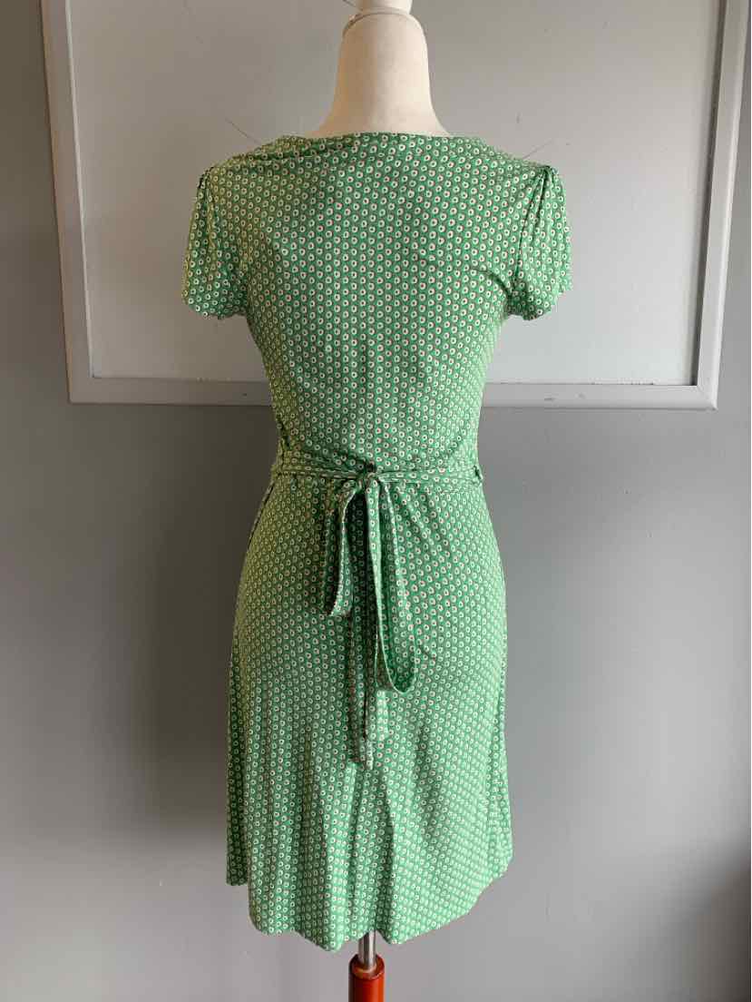 Green dress with white polka dots, short sleeves, and back tie waist on mannequin.