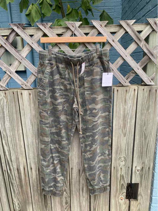 Green camouflage drawstring jogger pants with elastic cuffs hanging on wooden fence.