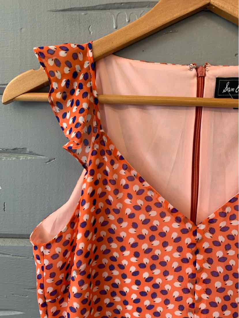 Sleeveless orange dress with ruffled straps and navy and white polka dots on fabric.