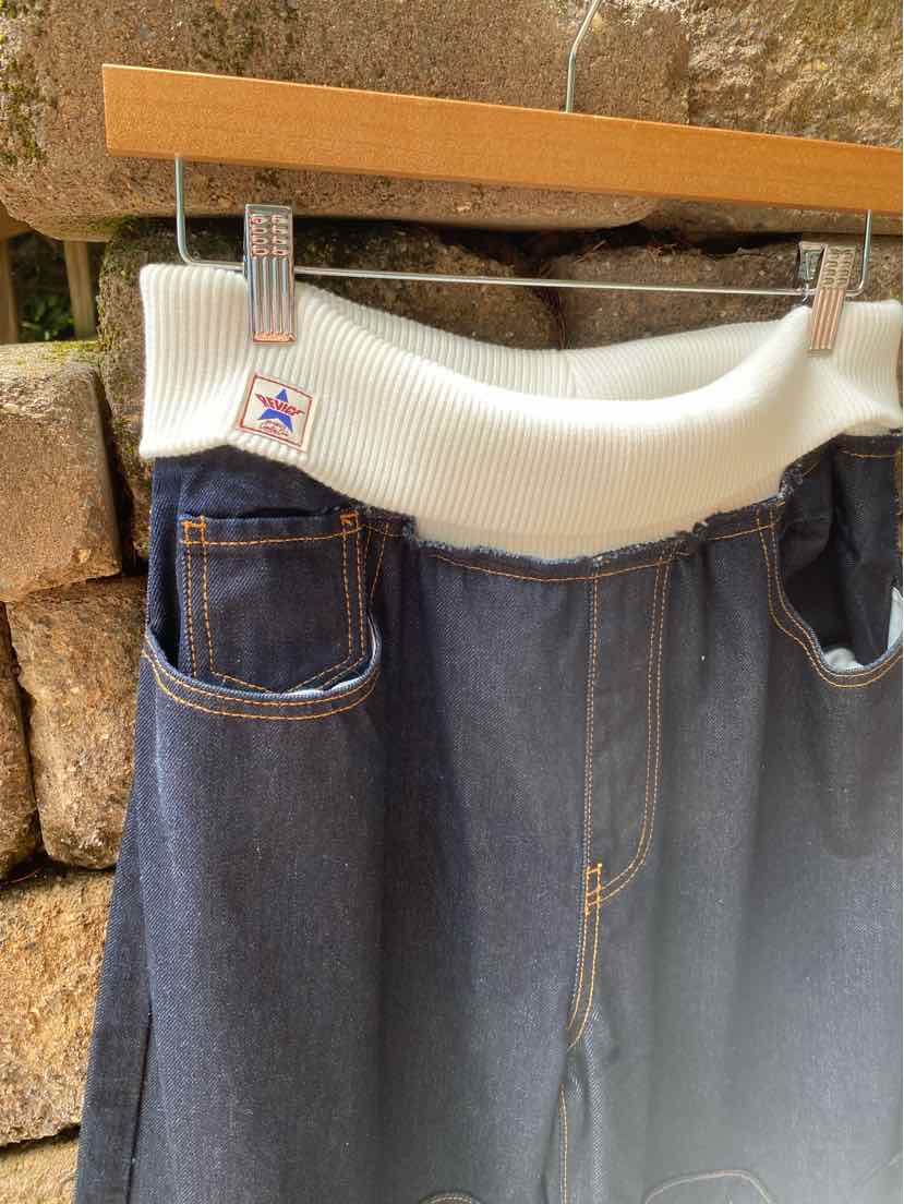 Dark blue denim skirt with white elastic waistband and front patch pockets hanging on wooden hanger.