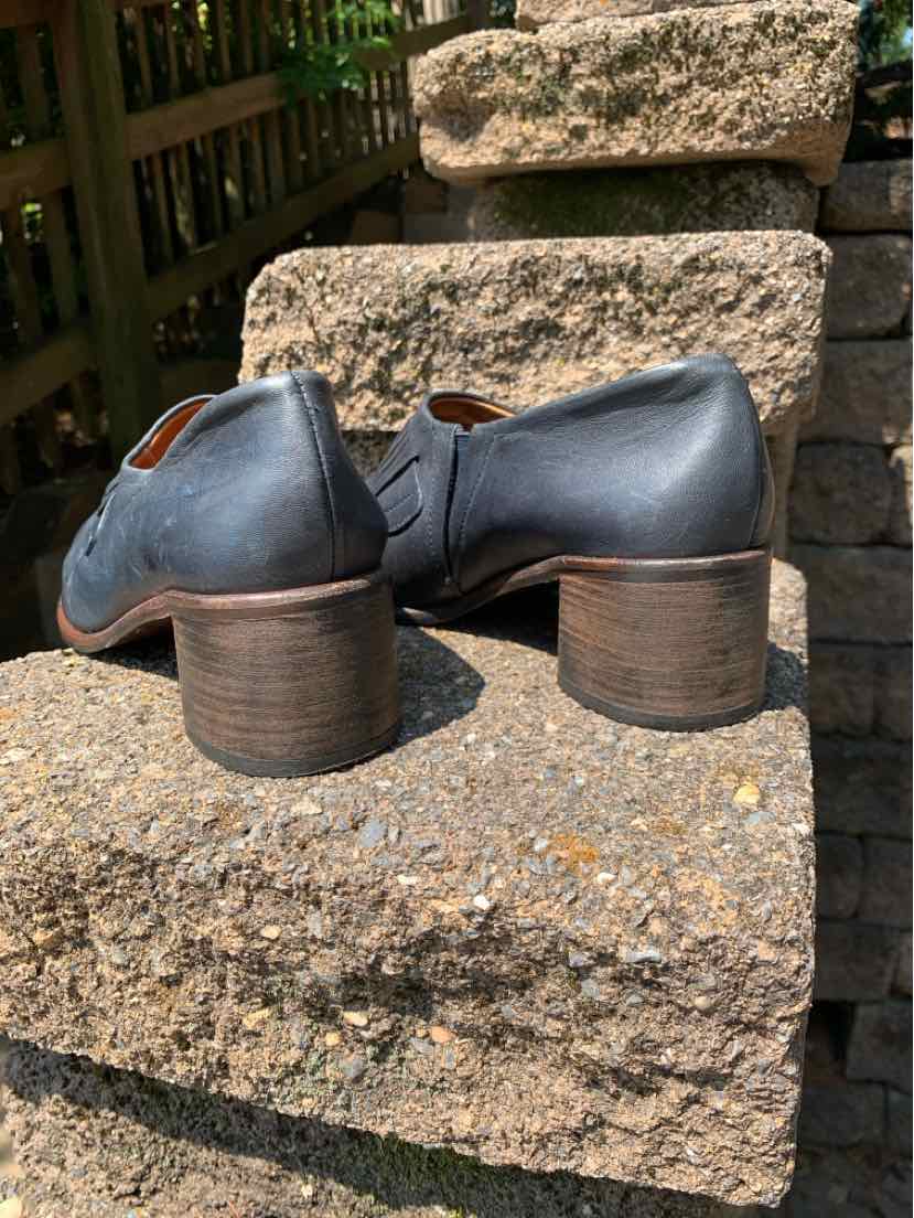 Black leather ankle boots with round toes and stacked block heels on stone steps.