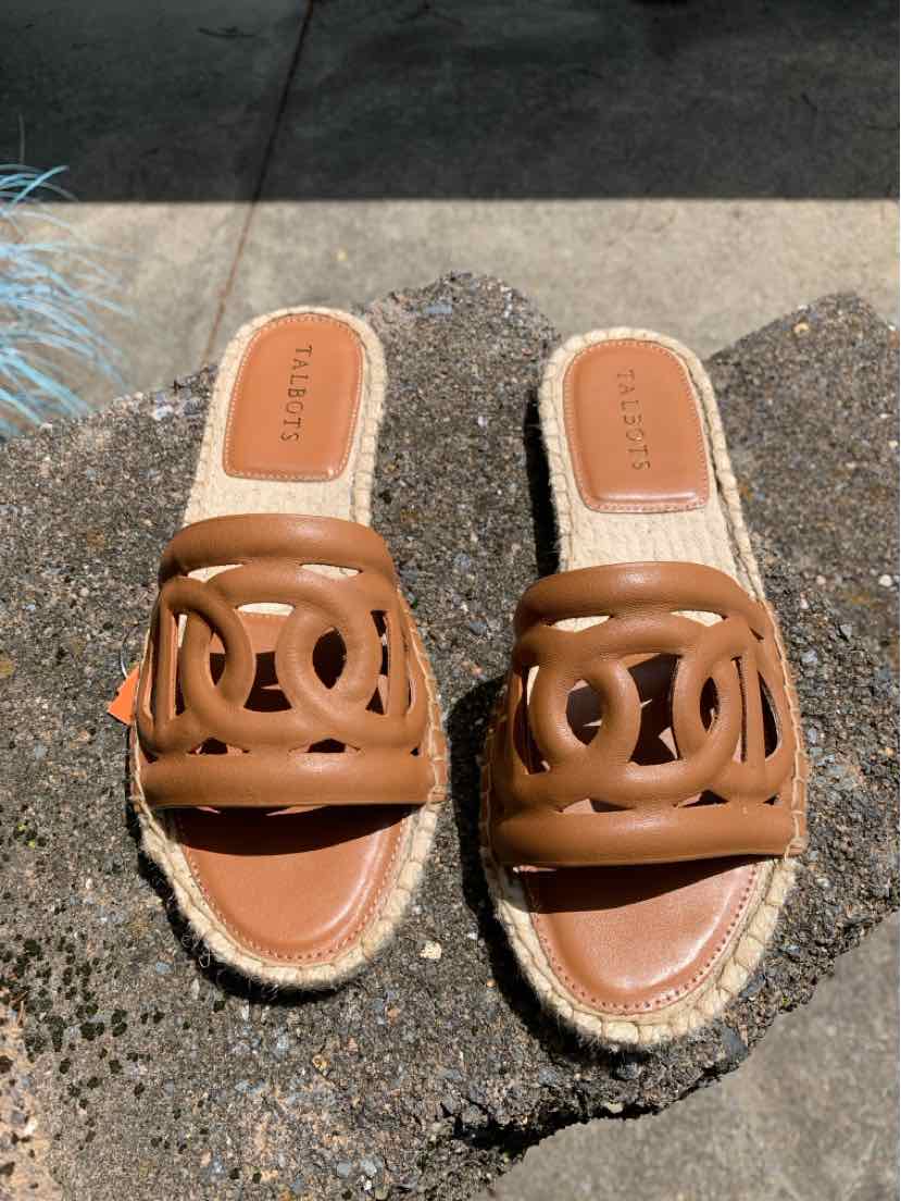 Tan leather slip-on sandals with open toe and decorative cutout design on woven espadrille sole.