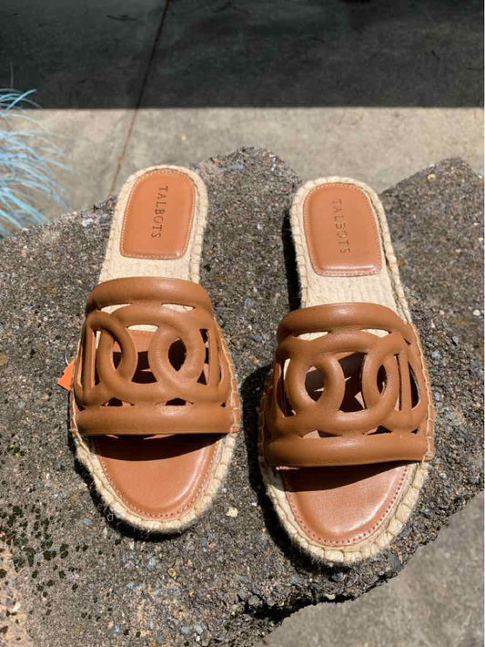 Tan leather slip-on sandals with open toe and decorative cutout design on woven espadrille sole.