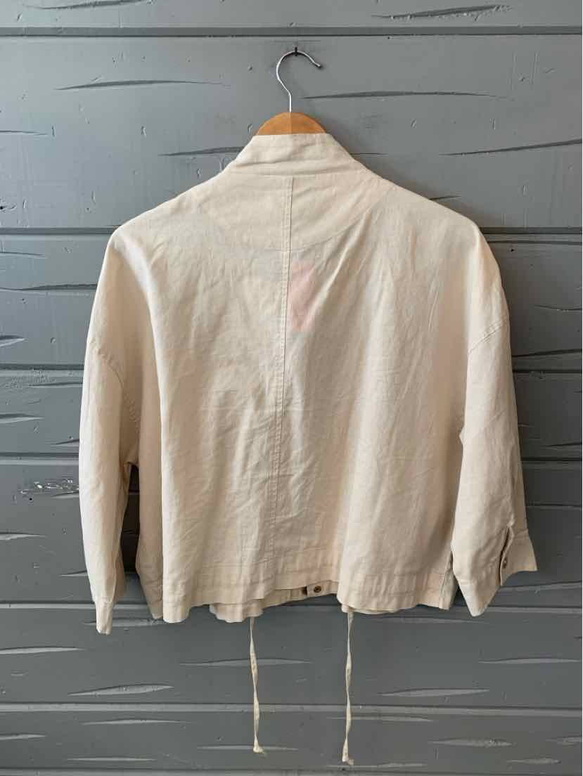 Cream-colored long-sleeve shirt with a collar, made from lightweight fabric, displayed on a wooden hanger.