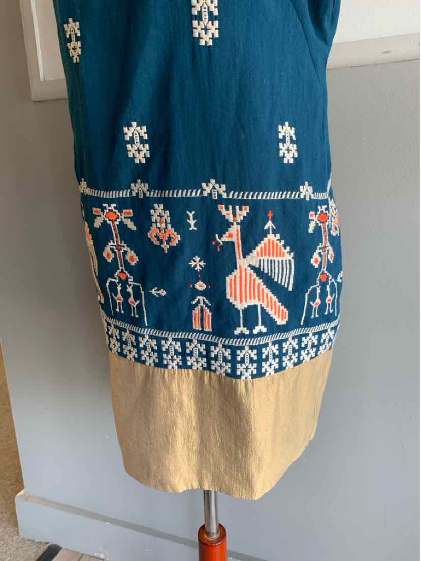 Blue fabric dress with embroidered white and orange tribal patterns and beige hem.