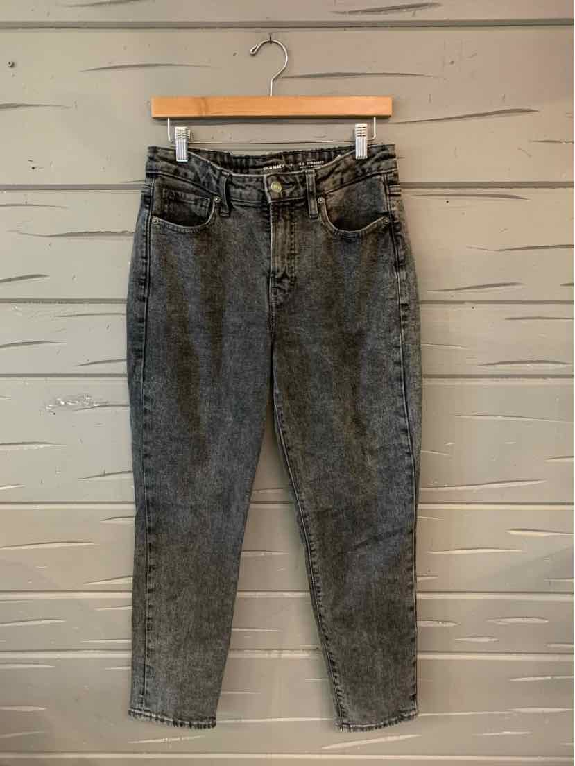 Black high-waisted denim jeans with tapered legs and front pockets hanging on wooden hanger.