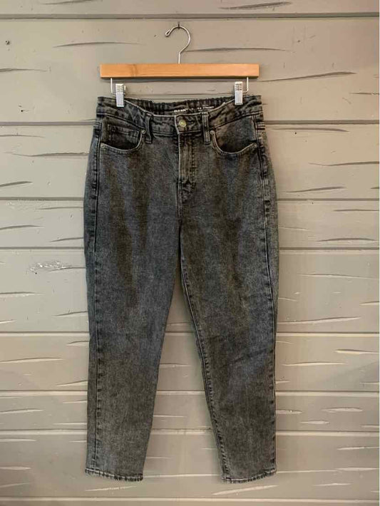 Black high-waisted denim jeans with tapered legs and front pockets hanging on wooden hanger.