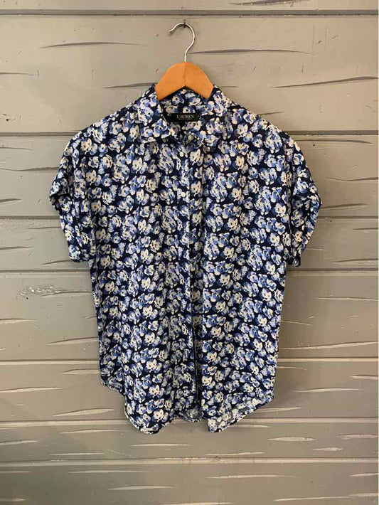 Navy blue short-sleeve button-up shirt with white floral print hanging on wooden hanger against beige wall.