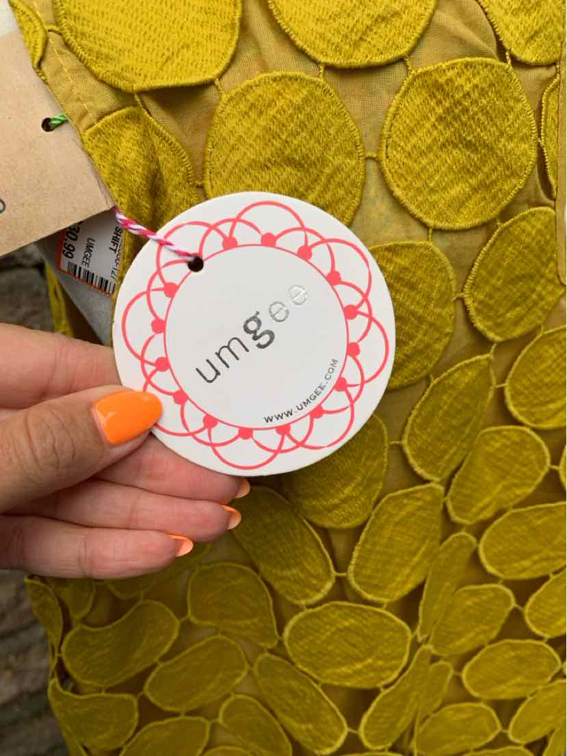 Close-up of yellow-green fabric dress with textured circular patterns and Umgee round brand tag held in hand with orange.