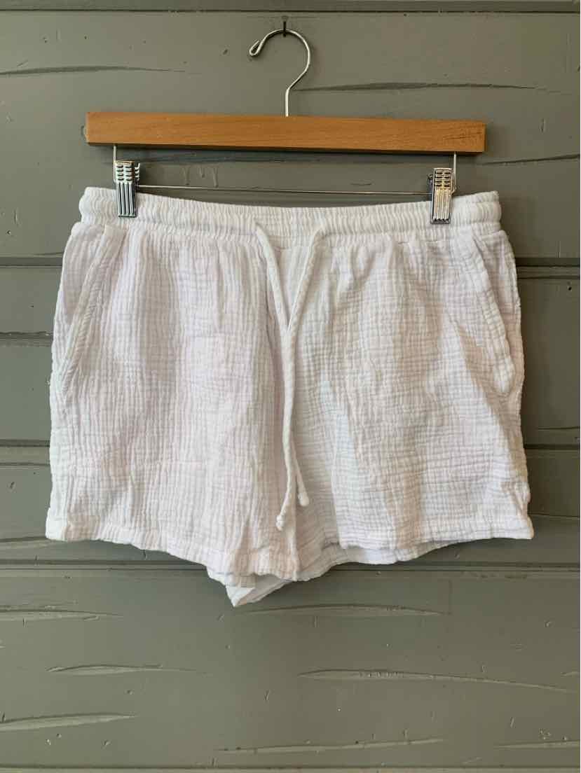 White textured cotton shorts with elastic waistband and side pockets hanging on wooden hanger.