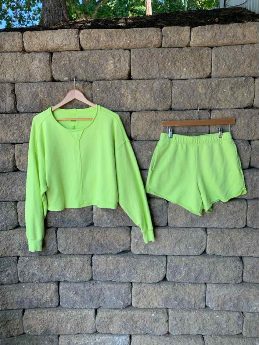 Light green long-sleeve cropped sweatshirt and matching soft shorts set hanging on wooden hangers against a stone wall.