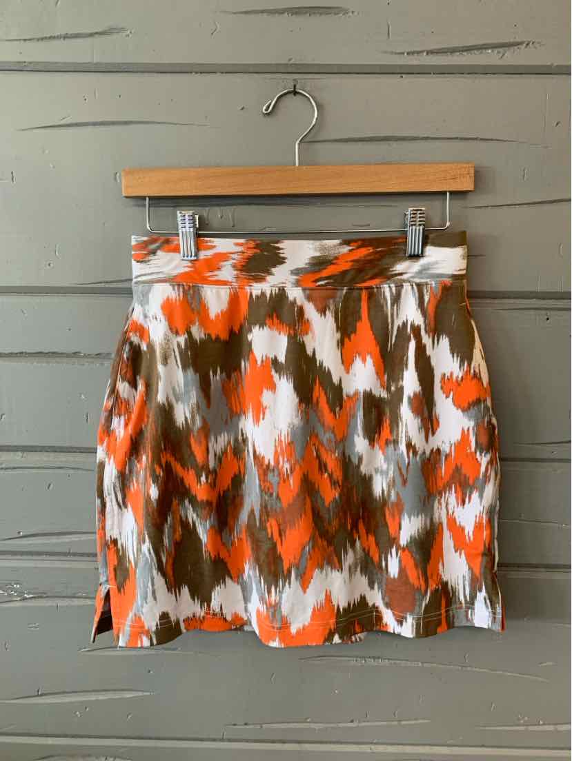 Orange, white, and brown abstract pattern pleated skirt hanging on wooden hanger against gray wooden wall.