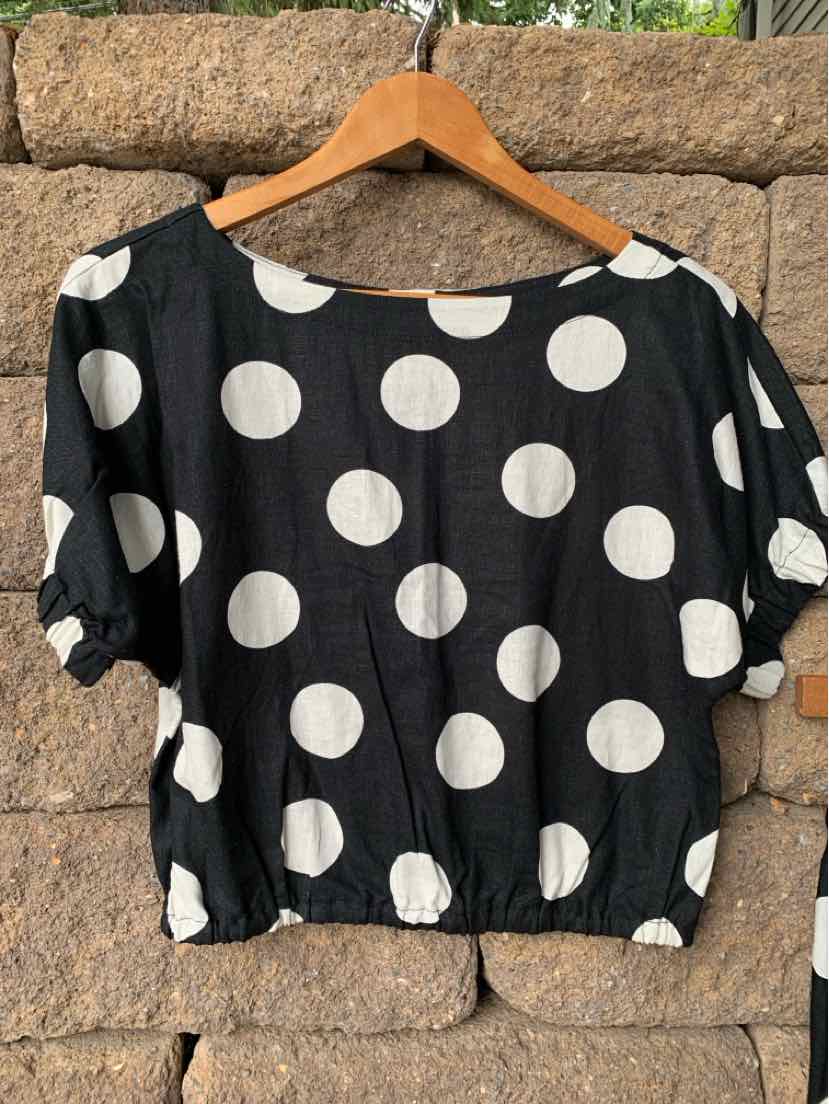 Black short-sleeve blouse with large white polka dots and gathered elastic hem.