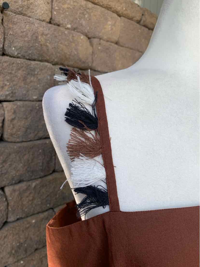 Brown sleeveless dress with fringe detailing in black, white, and brown on the shoulder straps.
