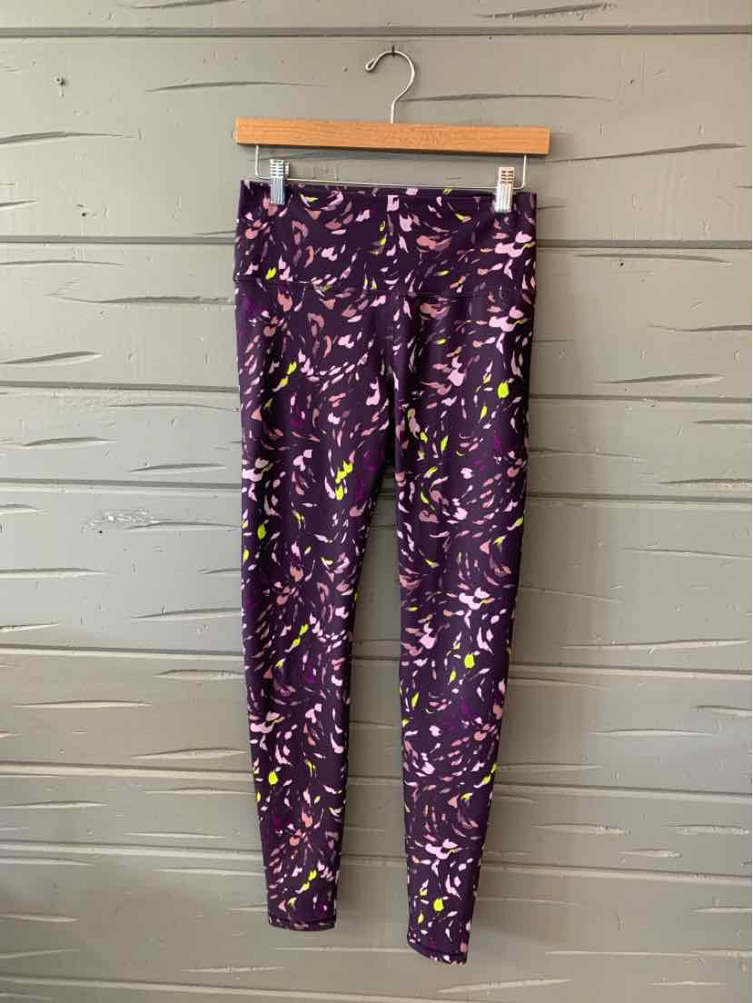 Purple leggings with colorful abstract leaf patterns, fitted style, medium size, hanging on wooden hanger.