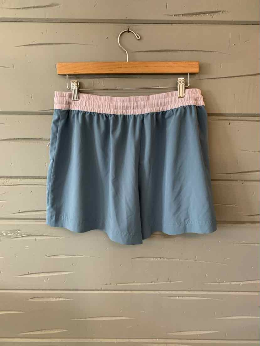 Light blue casual shorts with a soft pink elastic waistband hanging on a wooden hanger against a beige wall.