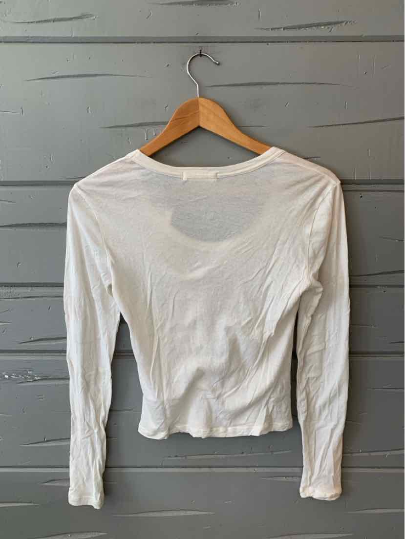 White long-sleeve fitted tee with crew neckline hanging on wooden hanger against gray wall.