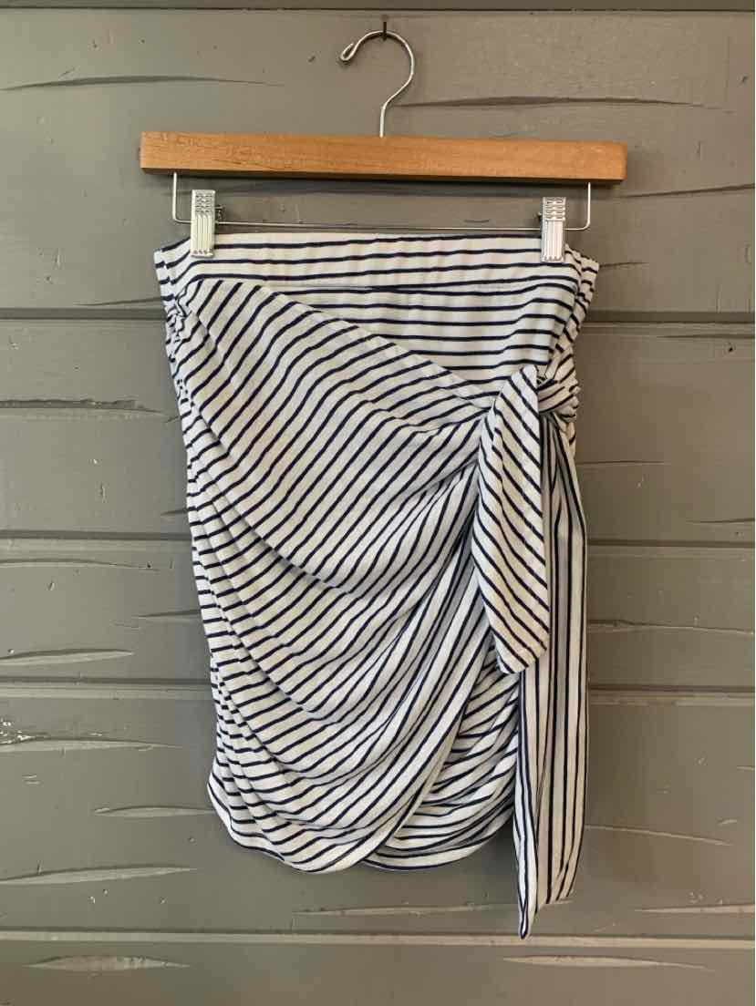 White mini skirt with black horizontal stripes and a gathered, draped side bow detail hanging on wooden hanger.