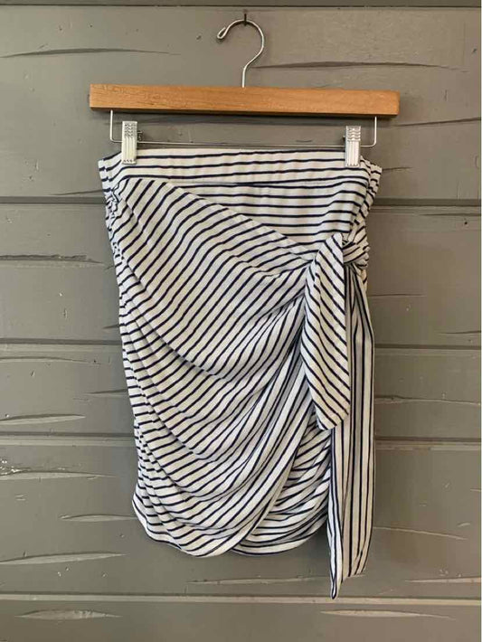 White mini skirt with black horizontal stripes and a gathered, draped side bow detail hanging on wooden hanger.